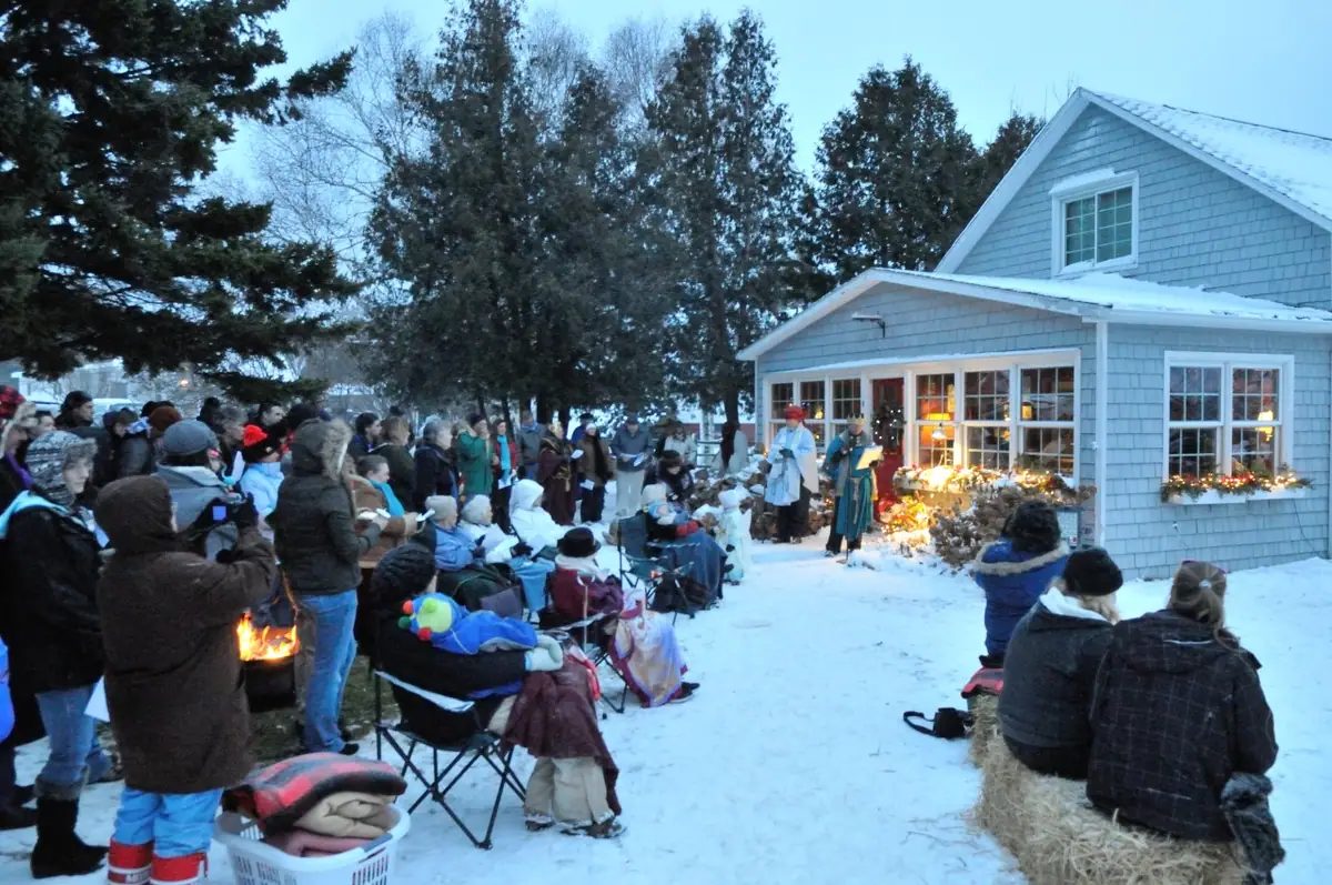 A winter outdoor gathering with robed participants, a fire, and seated spectators beside a house.