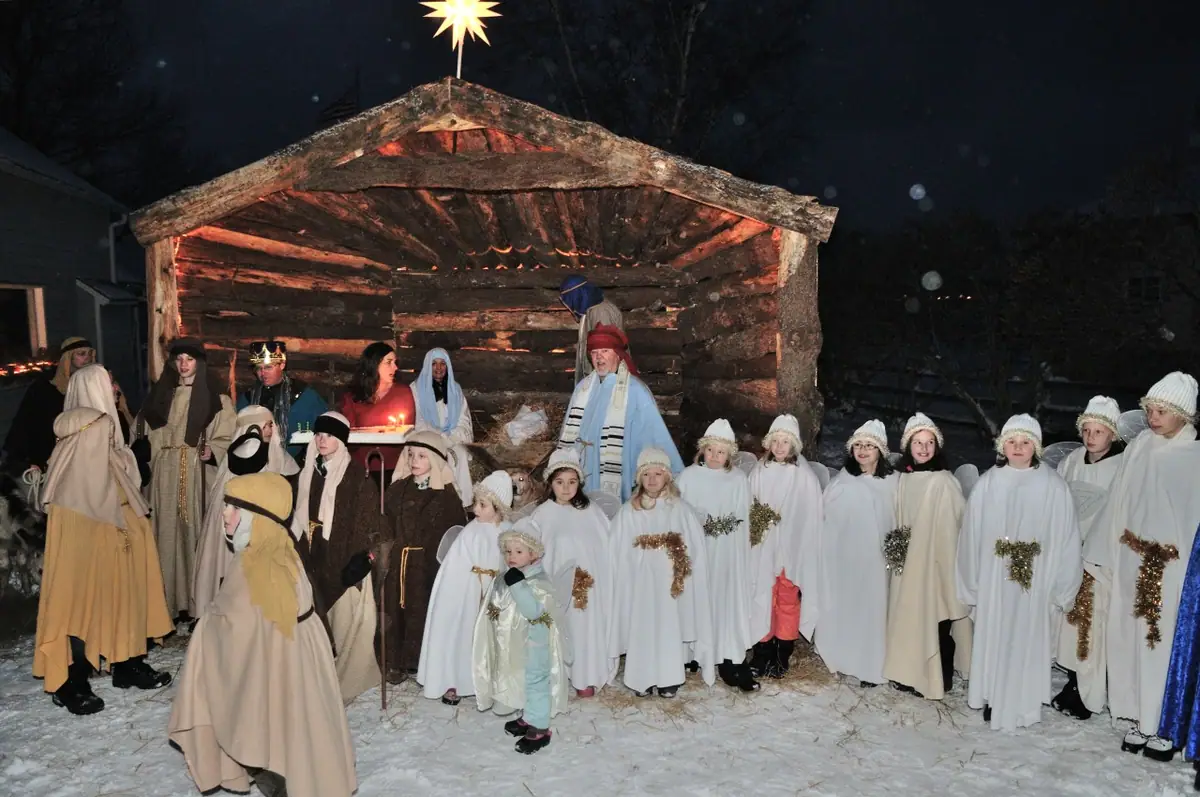 Adults and children in robes gather before a rustic shelter topped with a glowing star in the snow.