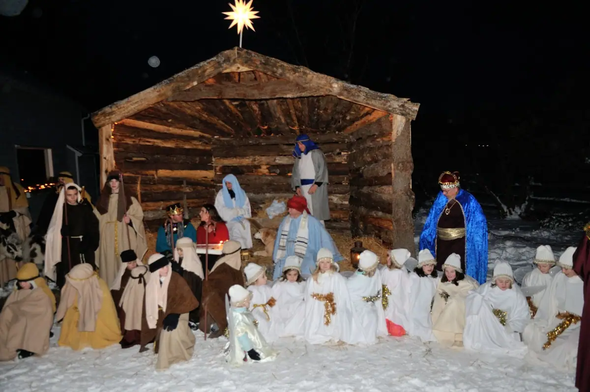 People in robes and white costumes pose in the snow beside a log shelter topped with a star.