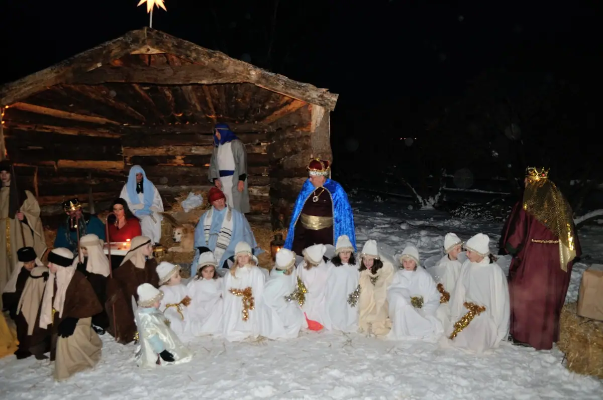 A costumed group gathers in snowy nighttime surroundings beside a rustic log shelter topped with a star.