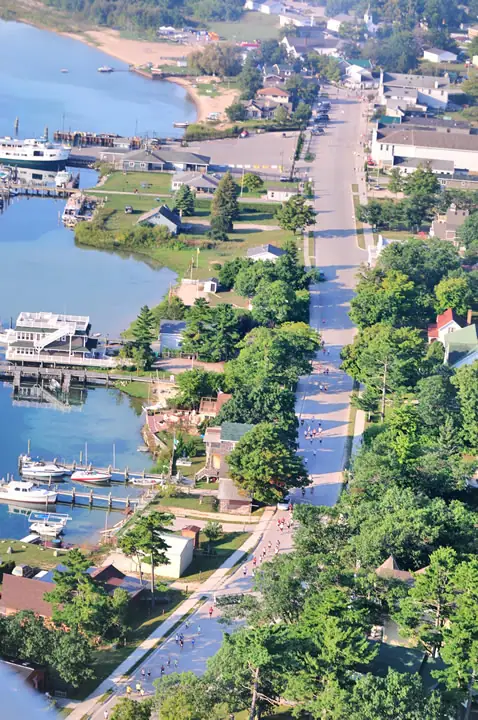 Aerial view of a waterfront town with boats, docks, streets, houses, and runners in a road race.