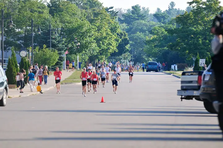 Runners move down a tree-lined street as spectators watch from the sidewalks.