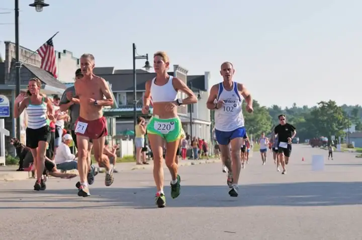 Runners wearing numbered bibs compete on a paved street lined with spectators and buildings.