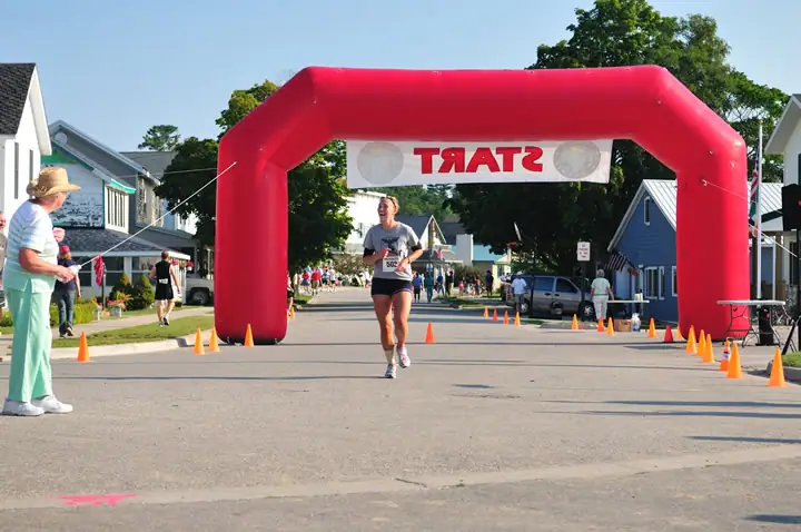 Runner passing beneath a red START arch on a residential street lined with traffic cones.