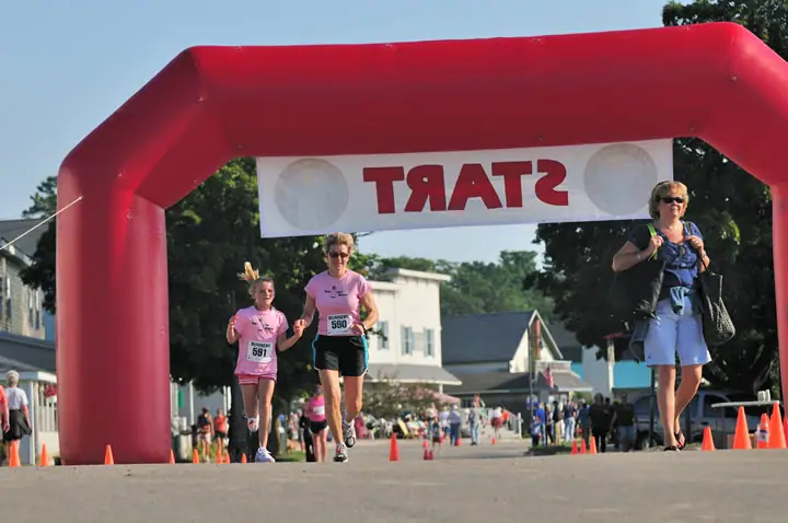 Two runners approach a red inflatable arch while spectators line a cone-marked street.