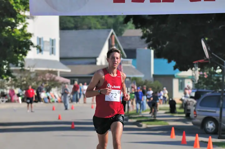 A runner wearing bib 72 competes on a cone-lined street as spectators watch.