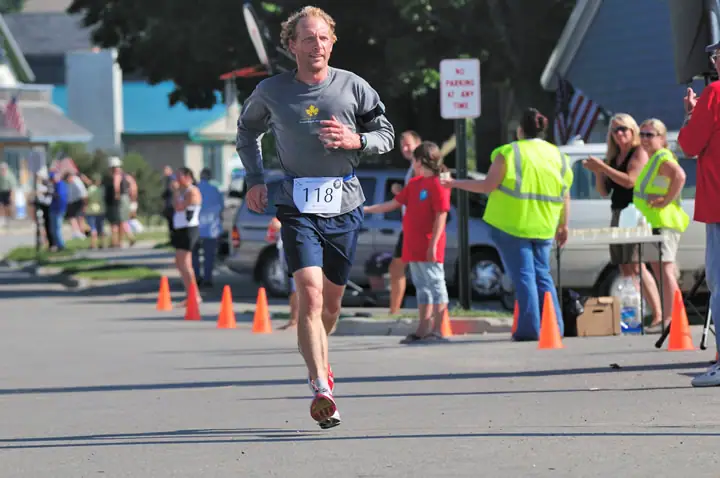 Runner 118 moves down a coned street as spectators and race volunteers watch.