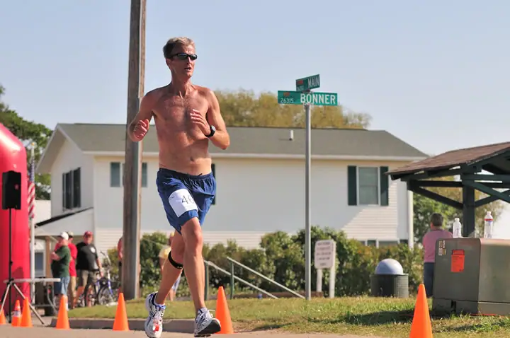 A shirtless runner passes traffic cones near a house and street signs.
