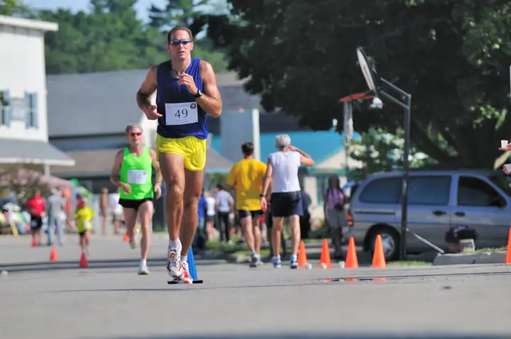 Runners move along a coned street while spectators and other participants gather behind them.