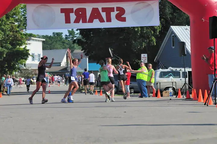 Runners pass beneath a red inflatable arch and white banner on a street.