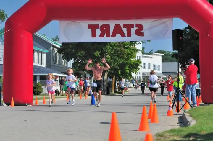 Runners pass beneath a red inflatable arch on a street lined with buildings and traffic cones.