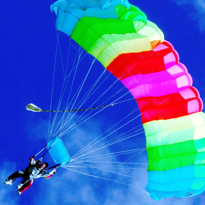 Two people descend beneath a brightly colored parachute against a deep blue sky.