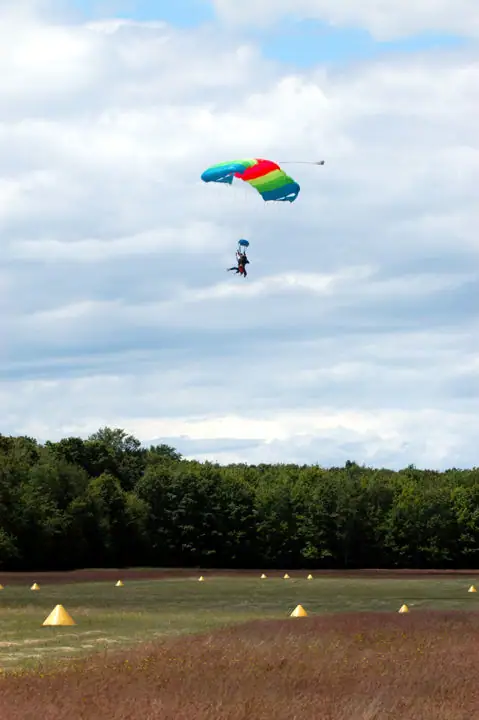 A parachutist descends beneath a bright multicolored canopy over a marked grassy field.