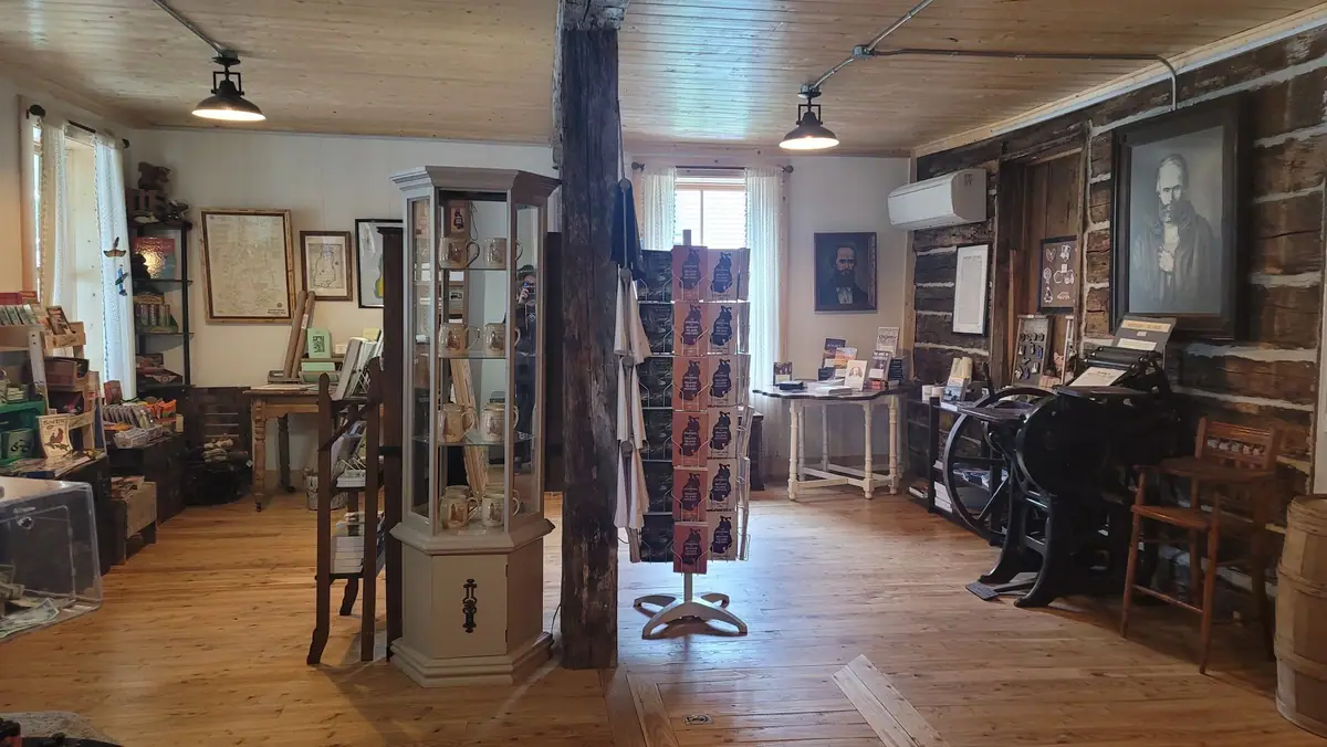 Wood-paneled historical shop interior with display cabinets, merchandise, framed documents, portraits, and antique equipment.