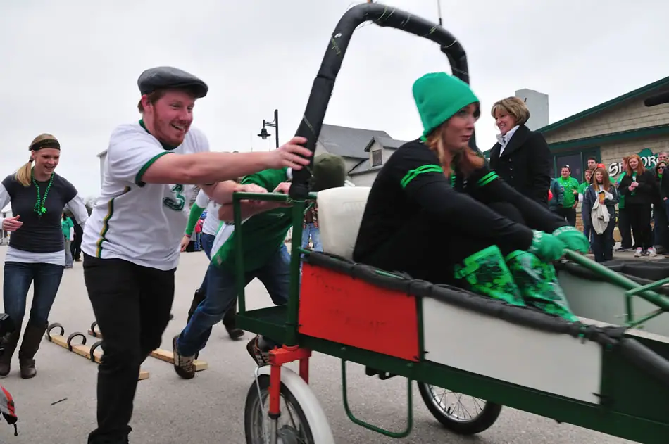People in green clothing take part in a street procession with a pedal-powered cart.