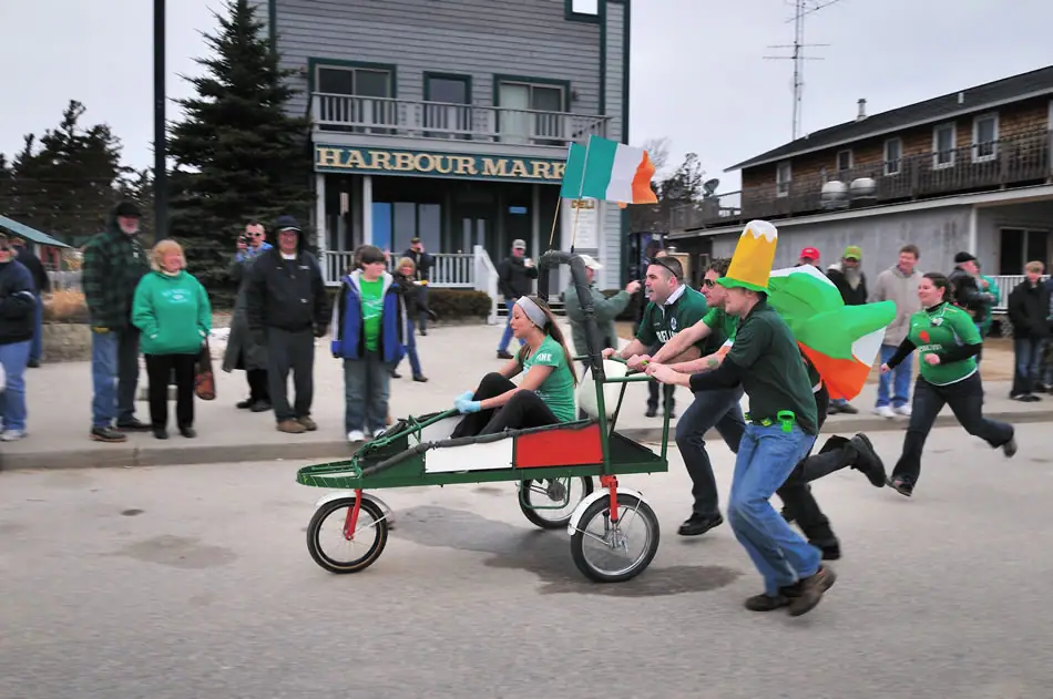 Participants run with a decorated handcart past spectators and the Harbour Market storefront.