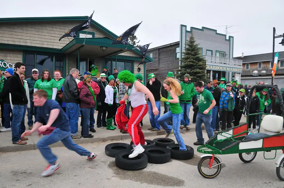 People in green gather around a tire obstacle on a decorated street.