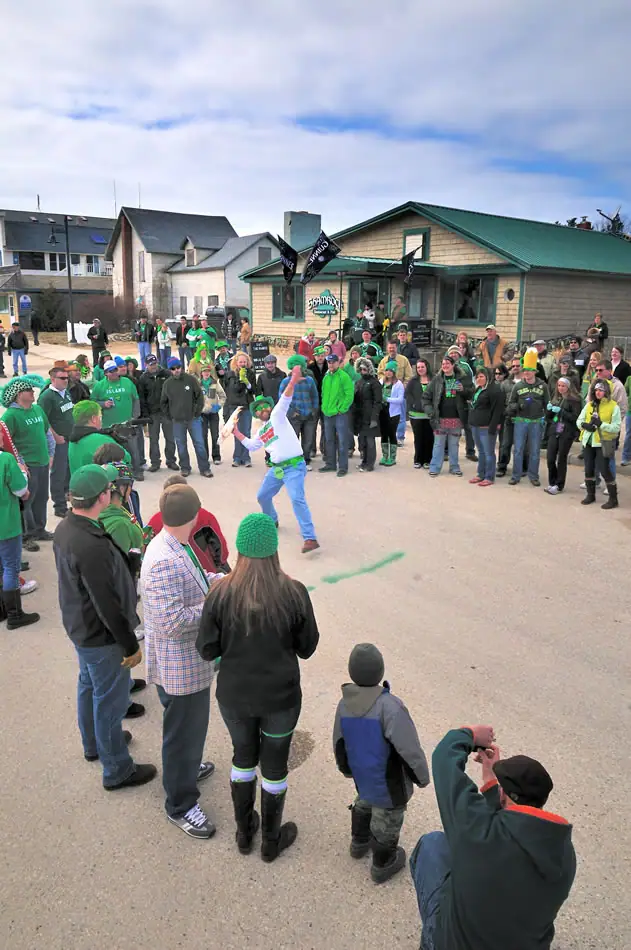 A crowd watches a dancer in bright clothing outside a low commercial building.