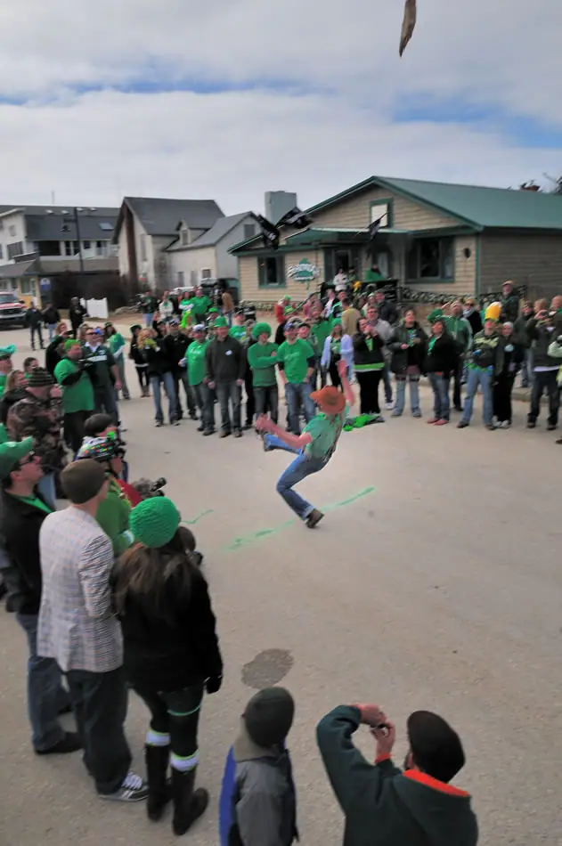 A costumed dancer performs before a crowd in a street lined with buildings.