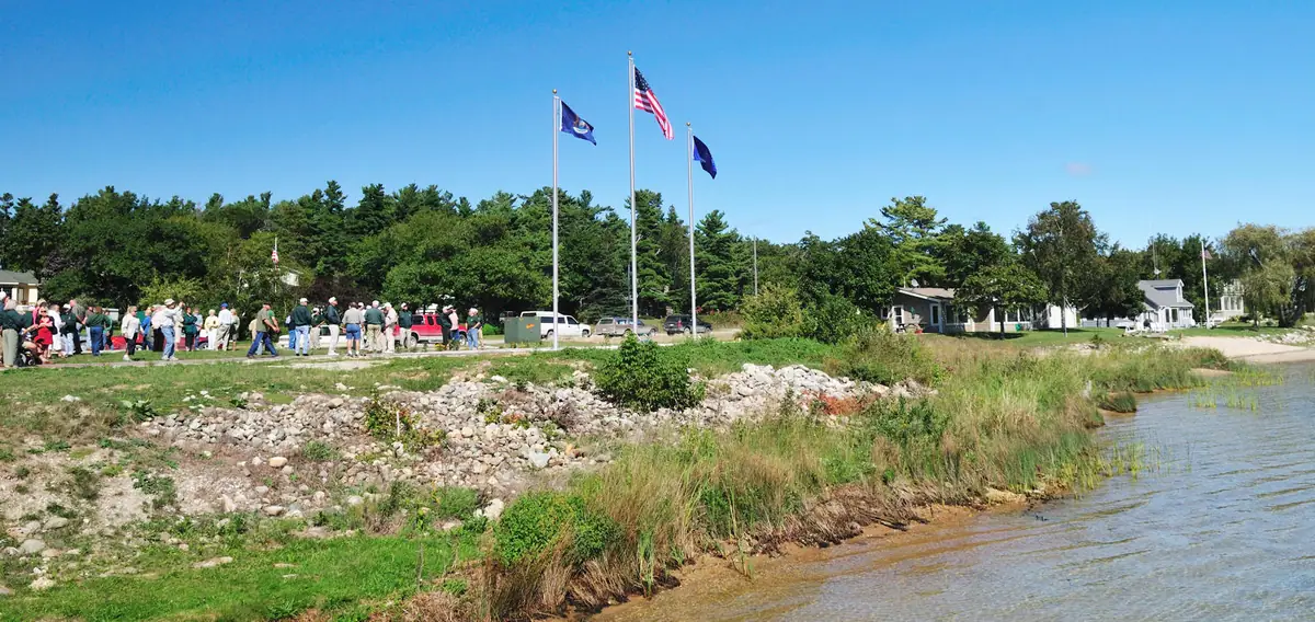 People gather beside flagpoles along a rocky shoreline.