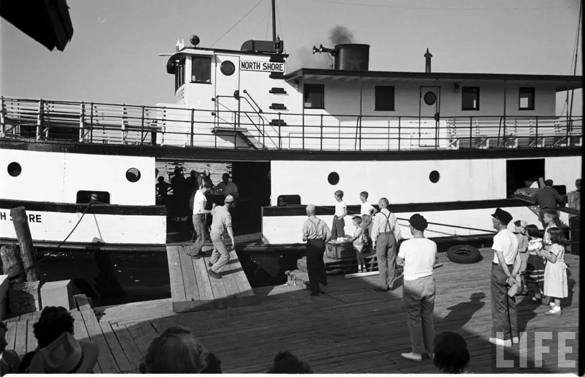 A ferry is docked beside a wooden pier as passengers and crew move between the vessel and shore.