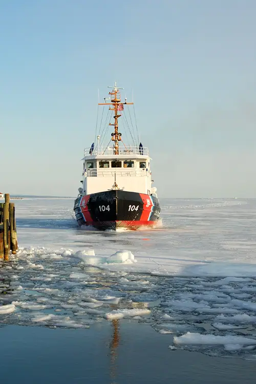 A tugboat marked 104 moves through broken ice toward a dock.