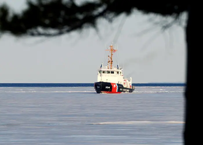 A red, white, and black vessel marked 104 moves through an ice-covered expanse, framed by dark branches.