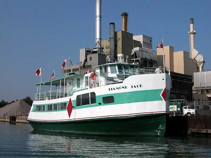Green-and-white ferry DIAMOND JACK is moored beside an industrial waterfront facility.