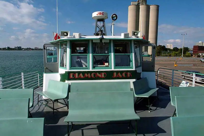 Ferry wheelhouse marked DIAMOND JACK, with passenger seating, water, and industrial silos behind it.