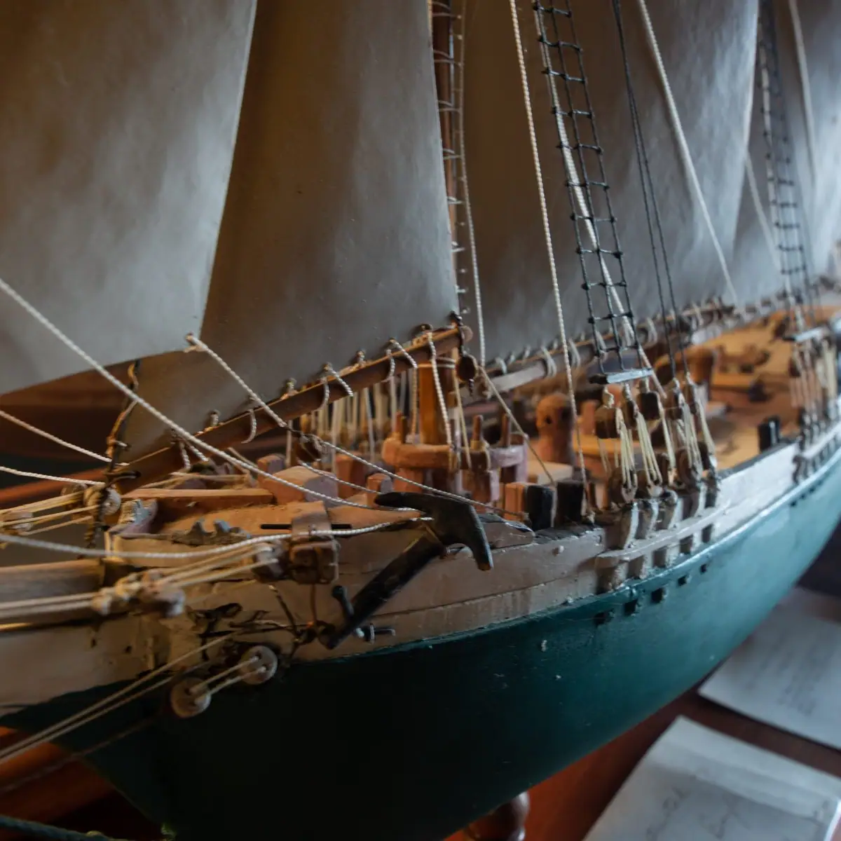 Close-up photograph of a detailed wooden sailing ship model with sails, rigging, and a dark-painted hull.