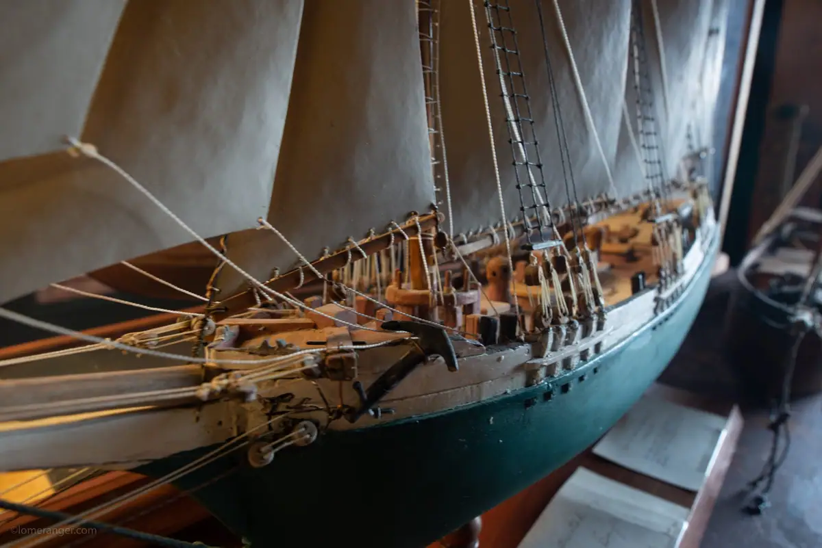 Close-up of a detailed wooden sailing-ship model with canvas sails, rigging, and a dark green hull.