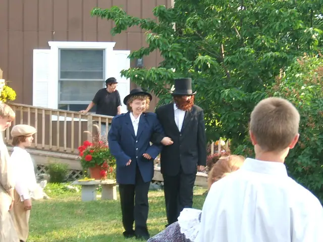Two adults in dark historical-style clothing walk arm-in-arm while children watch near a house.
