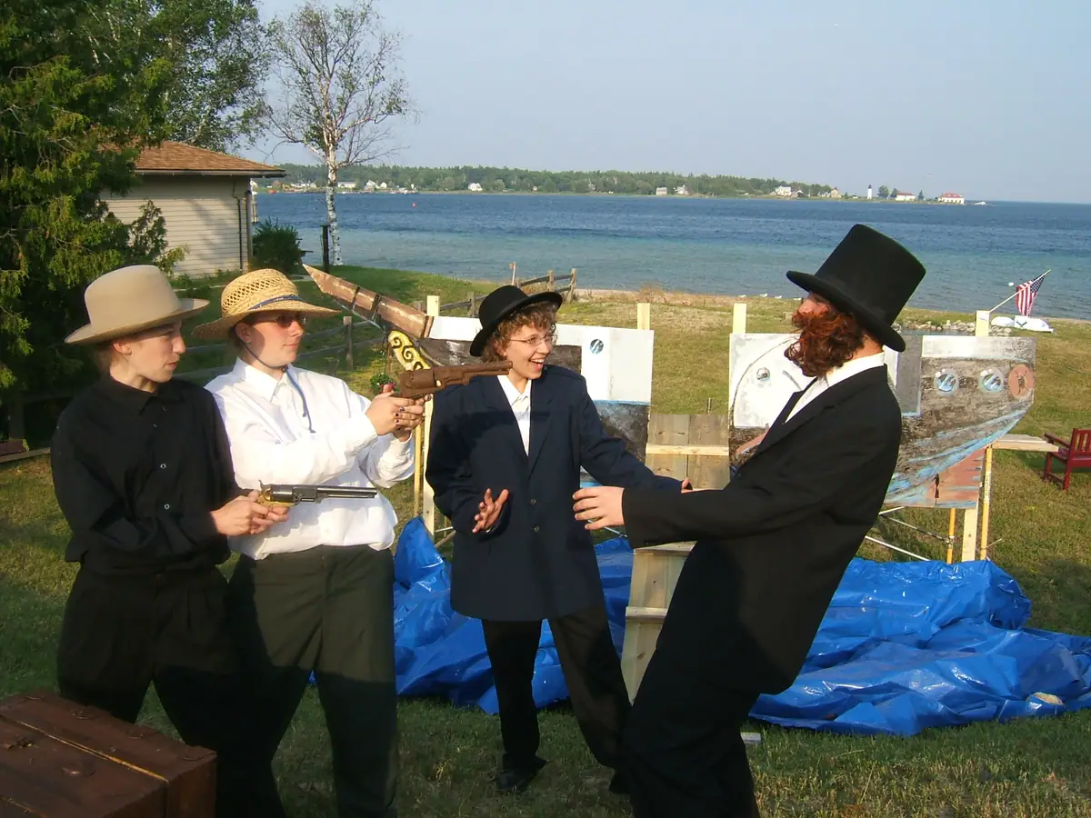 Four costumed performers pose with prop pistols beside a waterfront display.