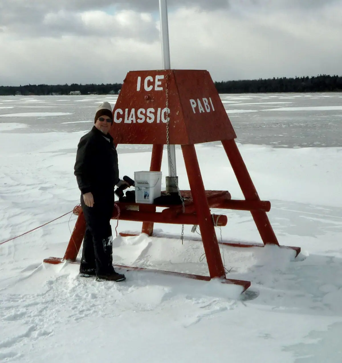 Person beside a red wooden structure marked “ICE CLASSIC” and “PABI” on snow-covered ice.
