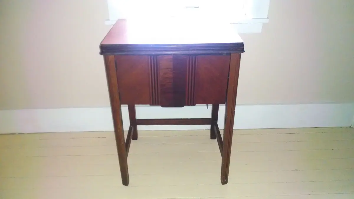 Dark wooden drop-leaf table standing against a pale wall beneath a window.