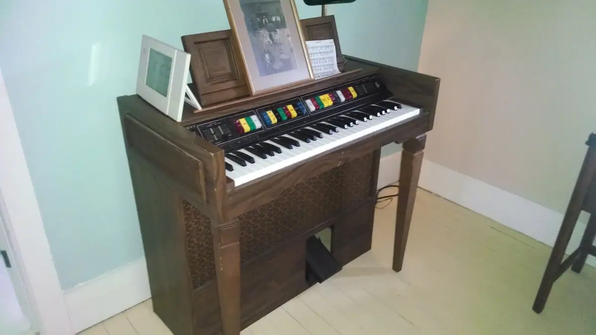 Wooden electronic keyboard with framed photographs and sheet music in an interior room.