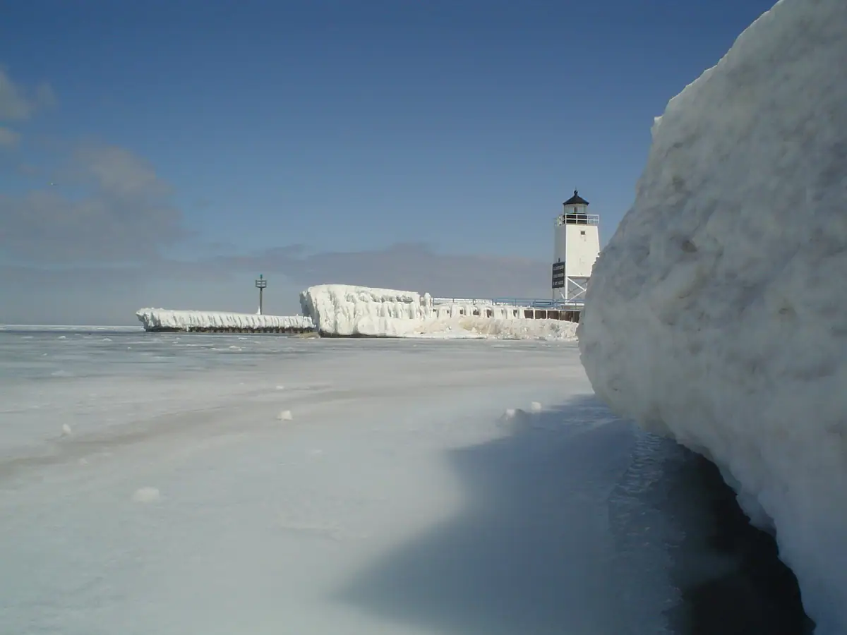 A lighthouse and ice-covered pier stand beside a frozen expanse of water.