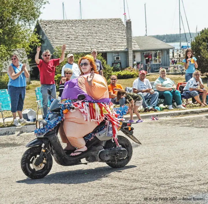 A costumed woman rides a decorated scooter past spectators during a parade.
