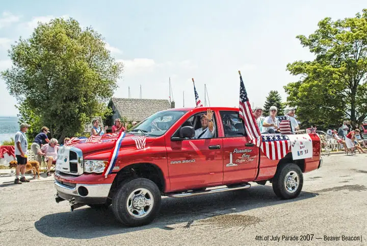 Red pickup decorated with flags carries riders in a street parade.