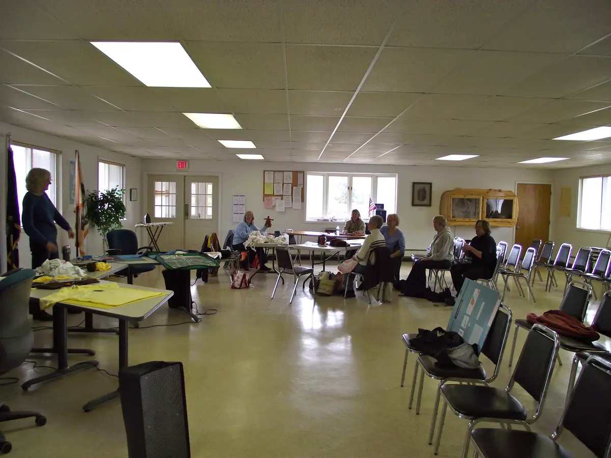 Adults work with fabric and craft materials around tables in a bright meeting room.