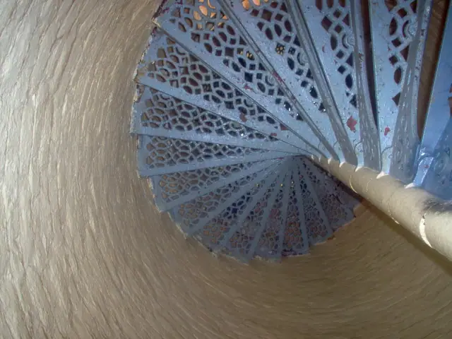 Looking down a blue perforated metal spiral staircase inside a round tower.