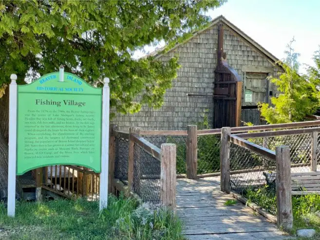 Shingled historic building beside an interpretive sign and a wooden accessibility ramp.