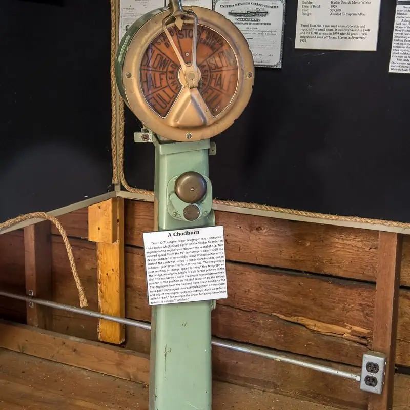 A brass engine-order telegraph mounted on a green-painted column in a wooden maritime exhibit.
