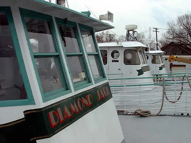 A white vessel with teal-trimmed windows and “DIAMOND JACK” painted on its cabin, with other boats behind it.