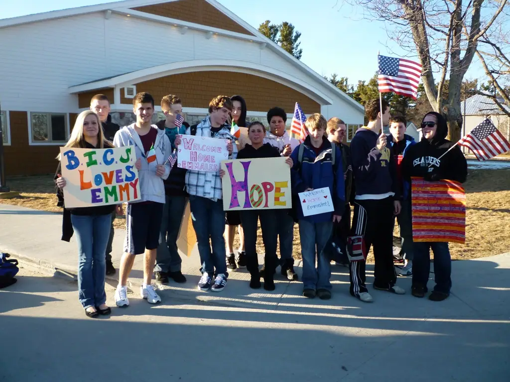 Young people pose outside a school building with handmade welcome signs and American flags.