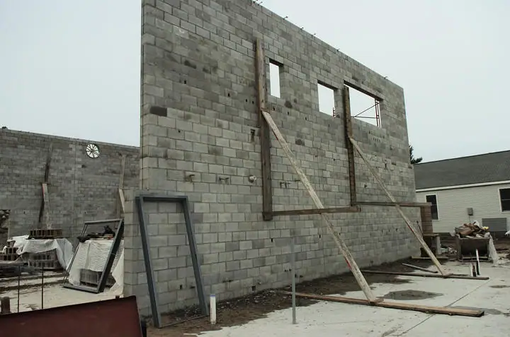 An unfinished concrete-block building with window openings, wooden braces, and construction materials.