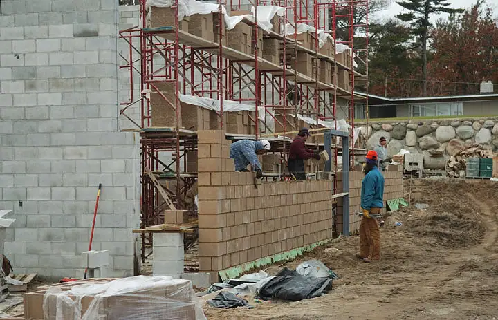 Workers build a block wall beside scaffolding at a construction site.
