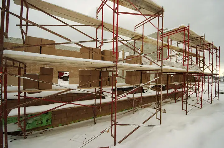 Snow-covered masonry building under construction, surrounded by red metal scaffolding.
