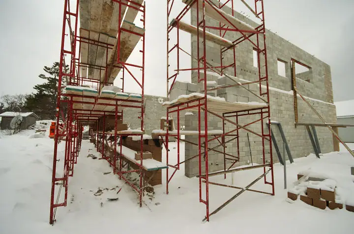 A concrete-block building rises amid red scaffolding and deep snow.