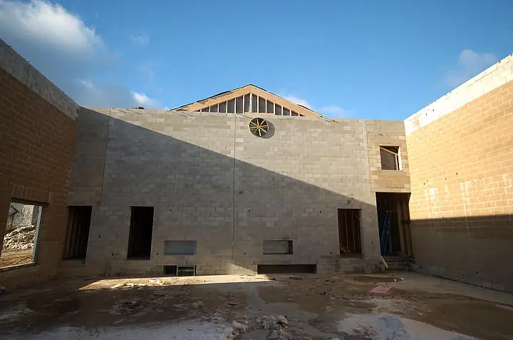 Unfinished building interior with concrete-block walls, brick side walls, exposed roof framing, and construction debris.